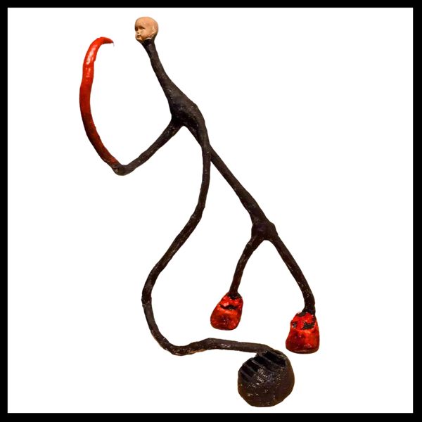 Looking at Me, Looking at You. A long, spindly figure with a tiny porcelain face, little red shoes and a weight trailing behind.